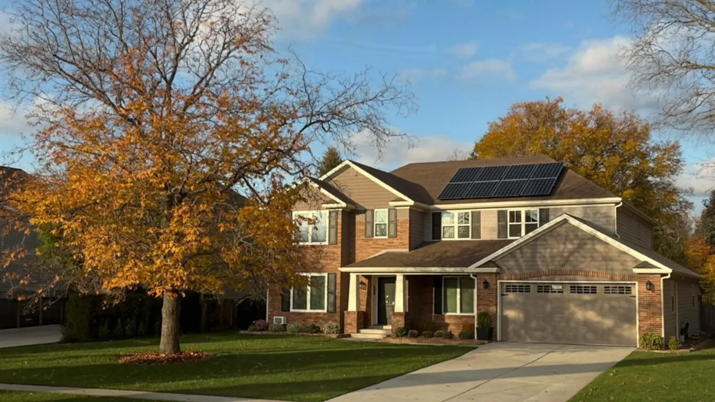 A newer brick home with black solar panels on its roof on an autumn afternoon.